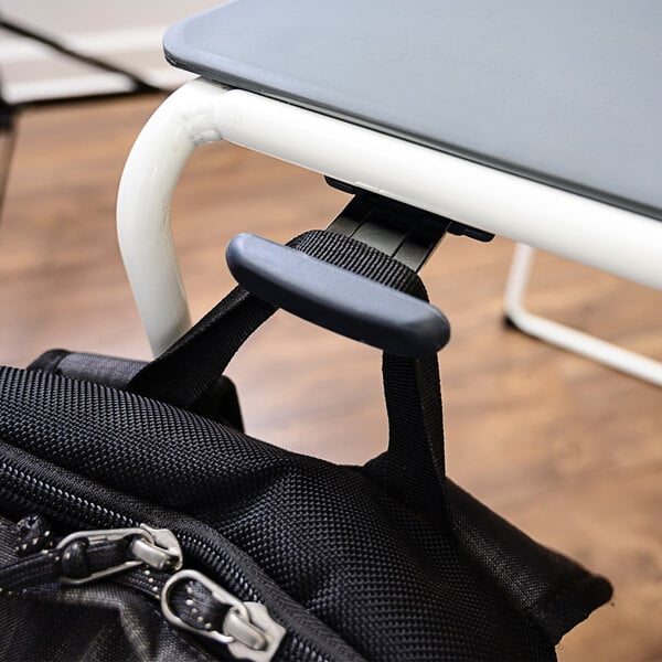 A black backpack hanging from a Luxor stackable chair at a desk.