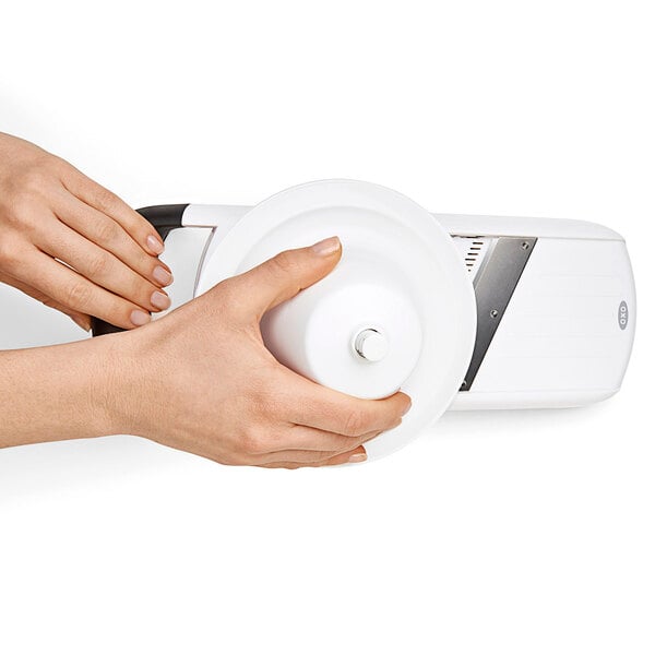 A person using an OXO white plastic mandoline slicer.