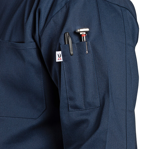A close up of a Uncommon Chef navy blue long sleeve chef coat with pockets.