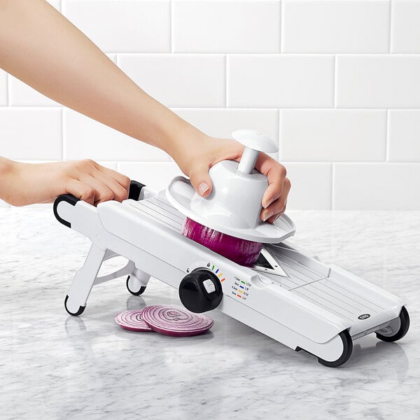 A person using an OXO mandoline slicer to slice a red onion.