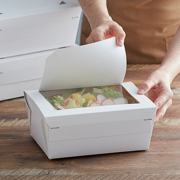 A person opening a Bio-Pak white paper take-out box with a window filled with food.