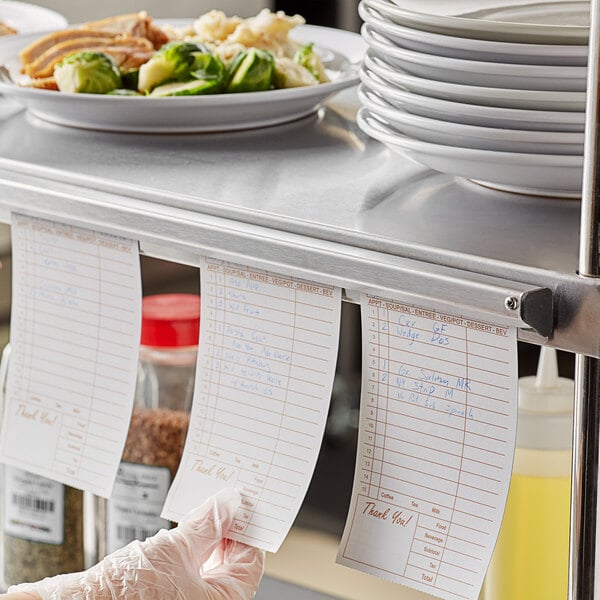 A person using an American Metalcraft stainless steel ticket holder to hold a paper with a list of food.