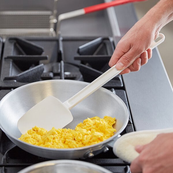 A hand using a Vollrath SoftSpoon to stir scrambled eggs in a pan.