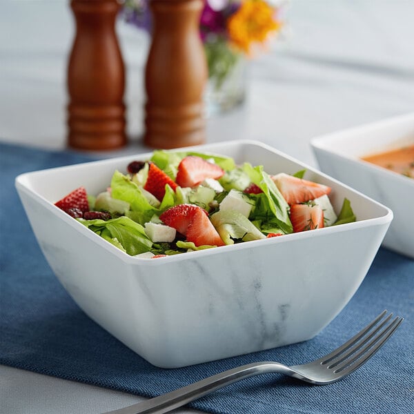 A bowl of salad with strawberries and cheese in a white American Metalcraft marble melamine bowl with a fork and knife.