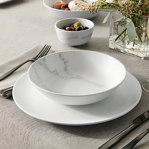 A white American Metalcraft matte round coupe plate with a bowl of olives on a table.