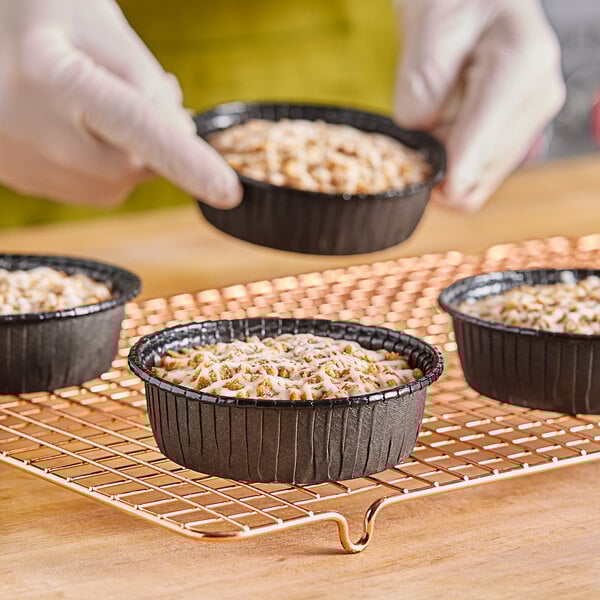 A person holding a tray of Solut black rolled rim baking cups filled with baked goods.
