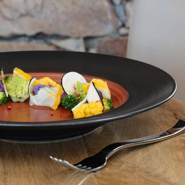 A RAK Porcelain walnut and black wide rim porcelain plate with food on a table.