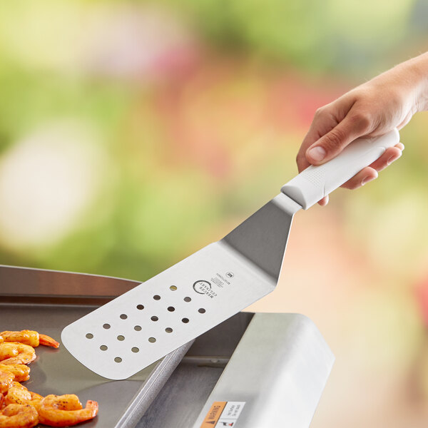 A hand using a Mercer Culinary Millennia Perforated Turner to grill shrimp.