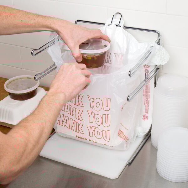 A person putting food into a white plastic "Thank You" bag.