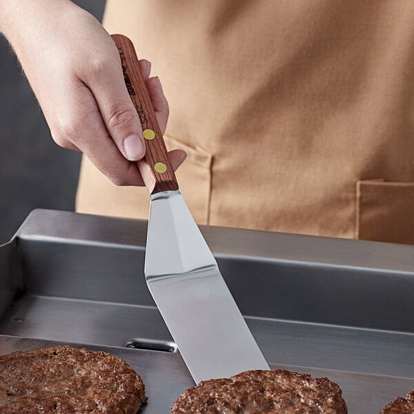A person using a Dexter-Russell Rosewood Turner to cook burgers on a grill.