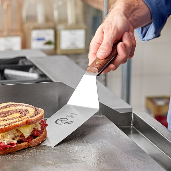 A person using a Mercer Culinary square edge turner to cut a sandwich on a counter.