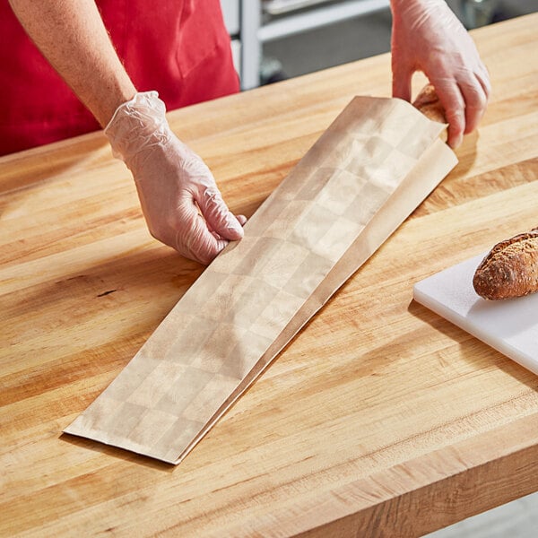 A person wearing red gloves using a Bagcraft Packaging bread bag to wrap a loaf of bread.