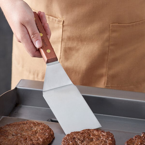 A person using a Dexter-Russell hamburger turner to cook burgers on a grill.