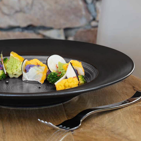 A grey and black RAK Porcelain Trinidad wide rim deep porcelain plate with food on it on a table.
