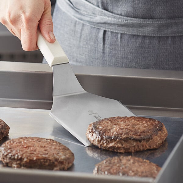 A person using a Dexter-Russell hamburger turner to cut a burger.