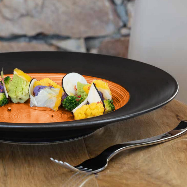 A RAK Porcelain Trinidad cedar and black porcelain plate with food on a table.
