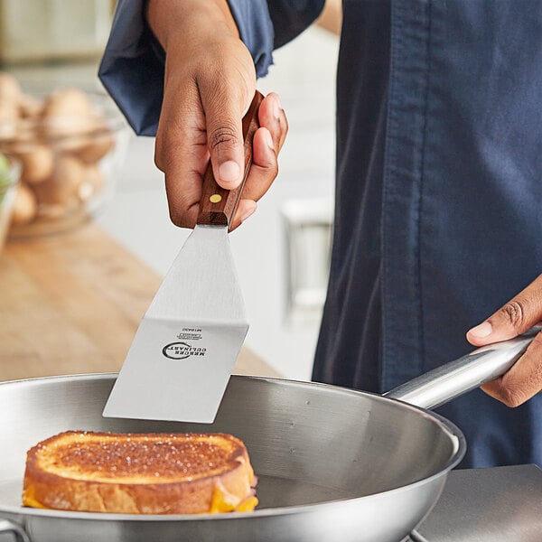 A person using a Mercer Culinary square edge turner to cut a sandwich.