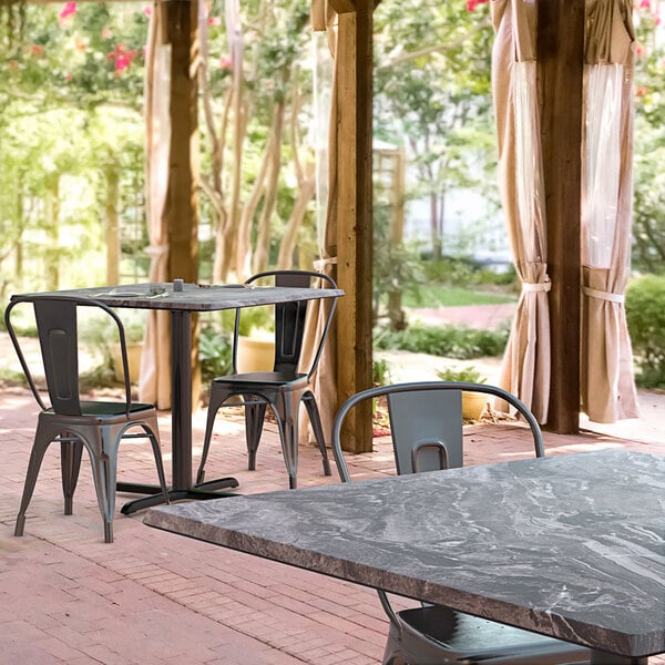 A Lancaster Table & Seating Excalibur square dining table with a smooth finish and cross base plate surrounded by chairs on a brick patio.