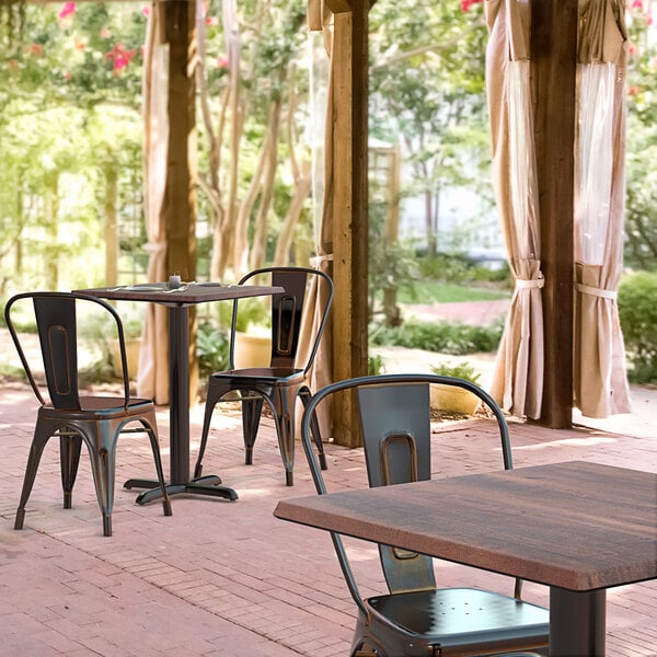 A Lancaster Table & Seating square table with a textured walnut finish and cross base plate on an outdoor patio.