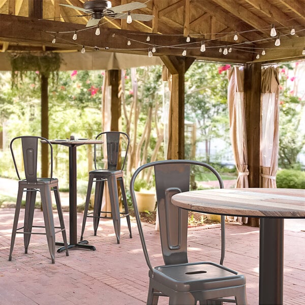 A Lancaster Table & Seating Excalibur wood table with a cross base plate and chairs on a covered patio.