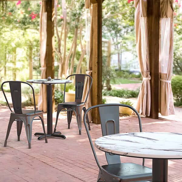 A Lancaster Table & Seating Excalibur round dining table with a cross base plate on an outdoor patio.