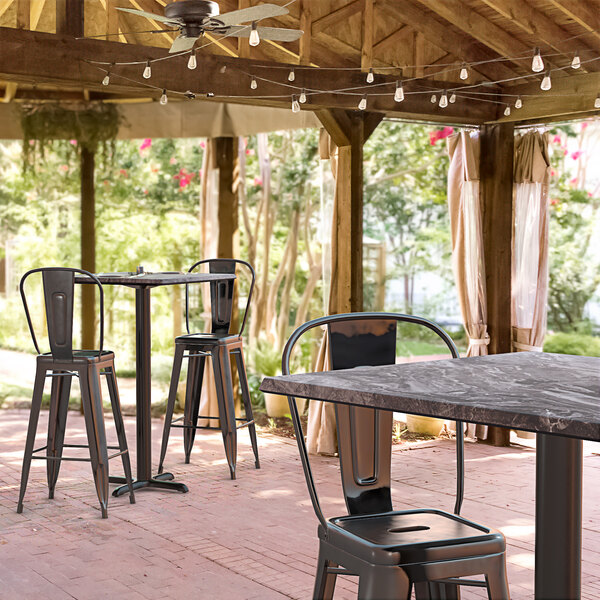 A Lancaster Table & Seating square bar height table with a smooth finish and cross base plate on a covered outdoor patio with chairs.