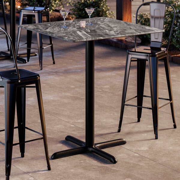 A square bar height table with a smooth paladina finish and a black cross base plate.
