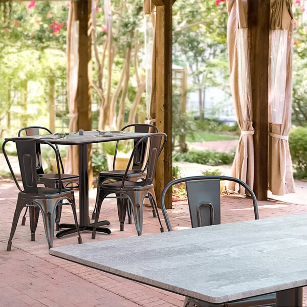 A Lancaster Table & Seating rectangular dining table with a textured Toscano finish and cross base plate on a patio with chairs.