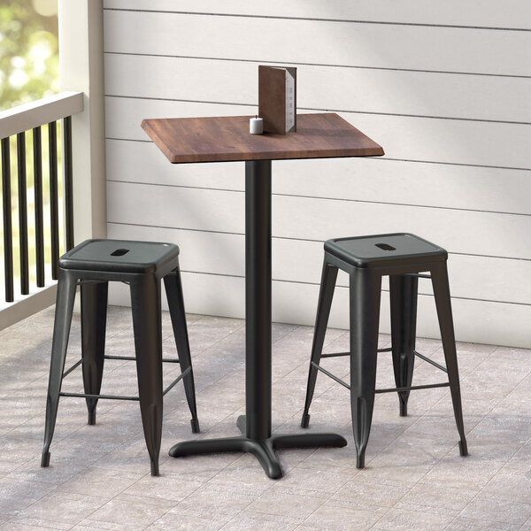 A Lancaster Table & Seating Excalibur square counter height table with a textured walnut finish and cross base plate on an outdoor patio.