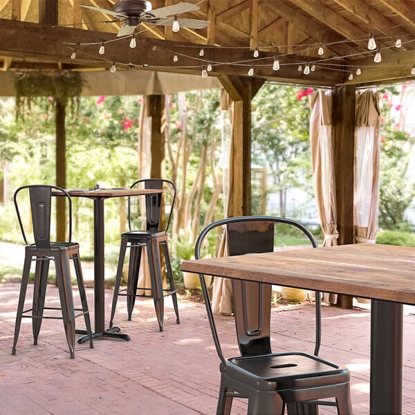 A Lancaster Table & Seating Excalibur bar height table with a textured Yukon oak finish on a covered patio.