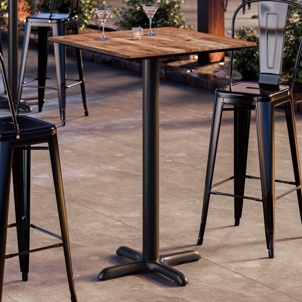 A square bar height table with a textured Yukon oak finish top and a black cross base plate.