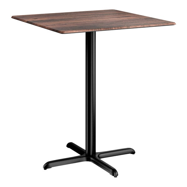 A square bar height table with a textured walnut finish top and a black cross base plate.