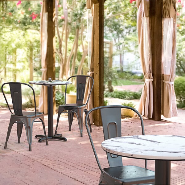 A Lancaster Table & Seating round dining table with a cross base on a patio with chairs.