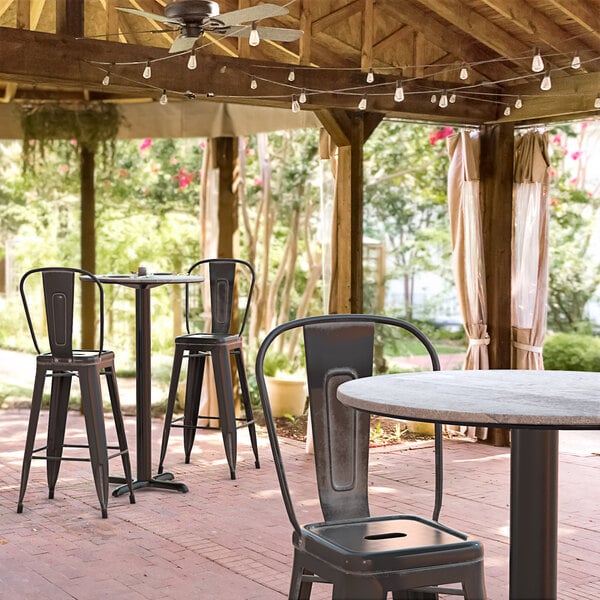 A Lancaster Table & Seating Excalibur bar height table with a textured Toscano finish and cross base plate on a patio with chairs.