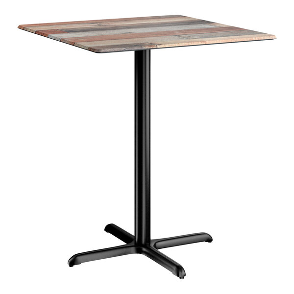 A square bar height table with a textured mixed plank finish top and a black cross base plate.
