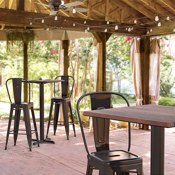 A Lancaster Table & Seating bar height table with a textured walnut finish and cross base plate on a covered outdoor patio.