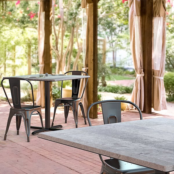 A Lancaster Table & Seating Excalibur square dining table with a cross base plate and two chairs on a brick patio.