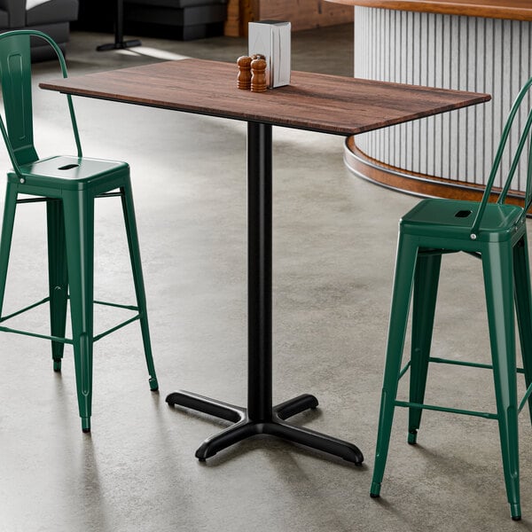 A rectangular bar height table with a textured walnut finish top and a black cross base plate.