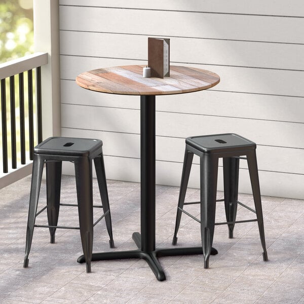 A Lancaster Table & Seating Excalibur round counter height table with textured plank finish and cross base plate with two stools on a porch.