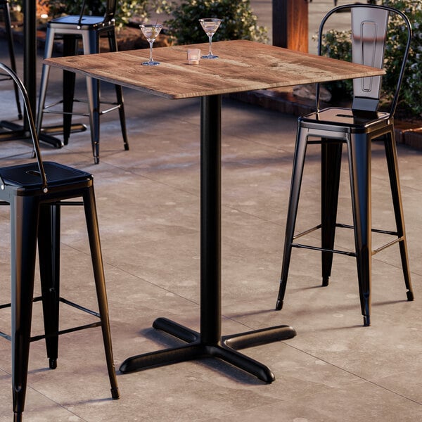 A square bar height table with a textured Yukon oak finish top and a black cross base plate.