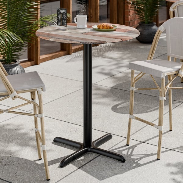 A round bar height table with a textured mixed plank finish top and a black cross base plate.