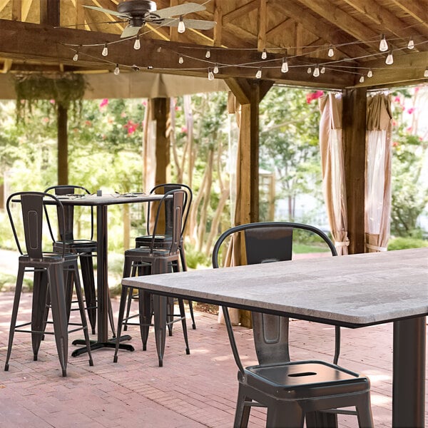 A Lancaster Table & Seating rectangular bar height table with a textured Toscano finish and cross base plate on a patio with chairs.