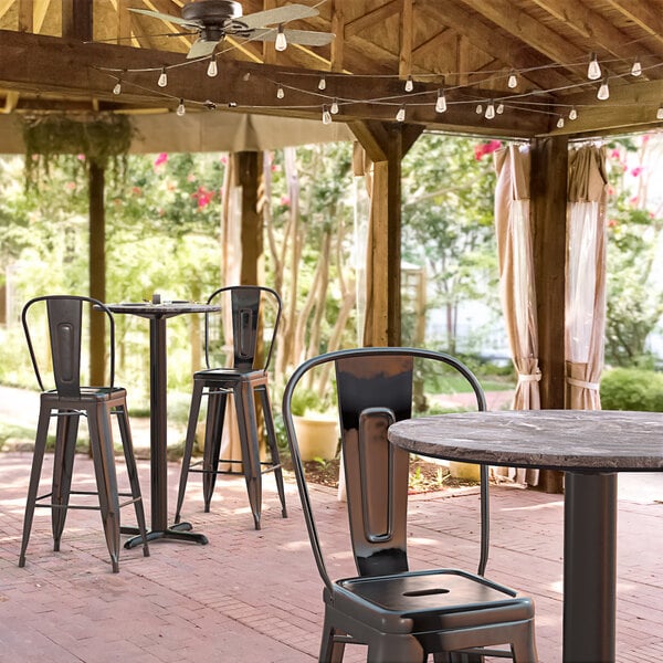 A Lancaster Table & Seating Excalibur bar height table with a Paladina finish and cross base plate on a brick patio.