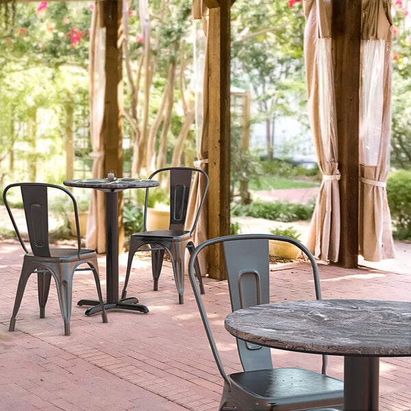 A Lancaster Table & Seating round dining table with a cross base plate and chairs on an outdoor patio.