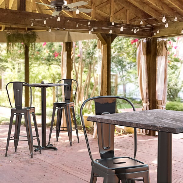 A Lancaster Table & Seating bar height table with a smooth finish on a covered patio with chairs.