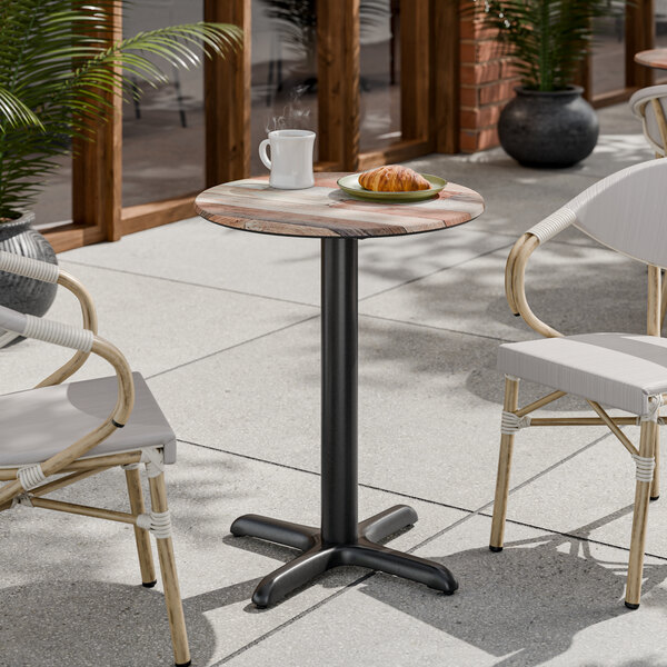 A round standard height table with a textured mixed plank finish and a black cross base plate.