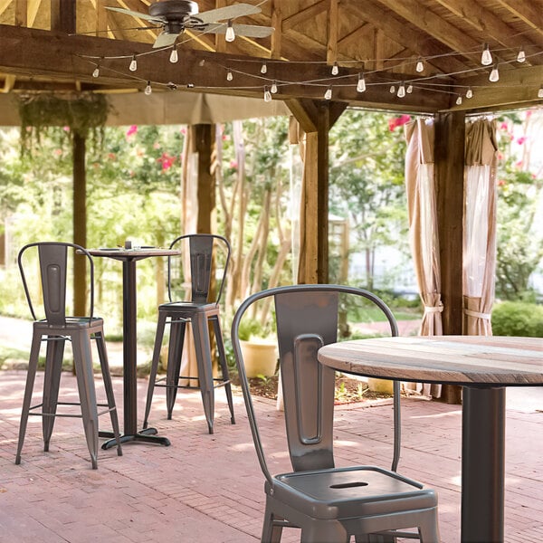 A Lancaster Table & Seating round bar height table with a textured mixed plank finish and cross base plate on an outdoor patio.