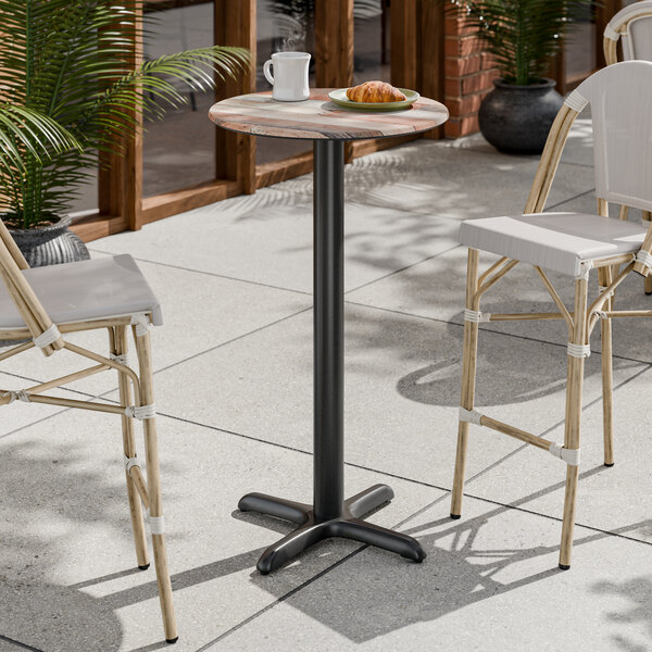 A round bar height table with a textured mixed plank finish top and a black cross base plate.
