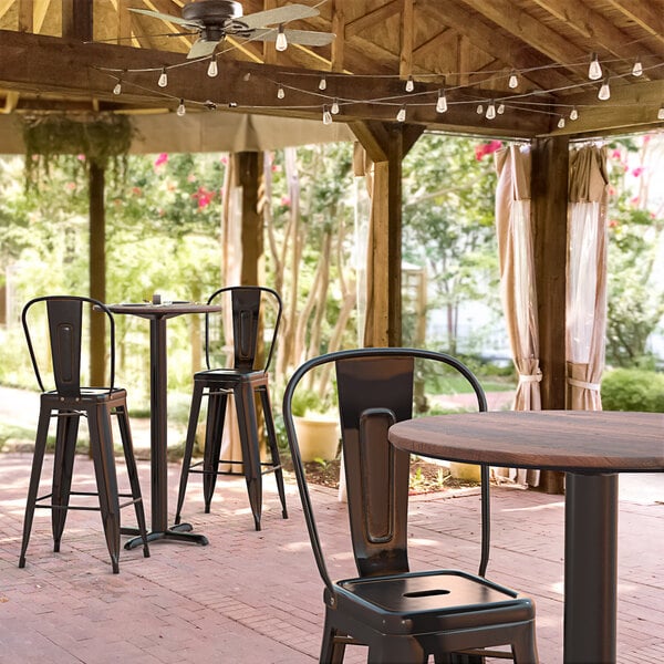 A Lancaster Table & Seating bar height table with a textured walnut finish and cross base plate on a brick patio.