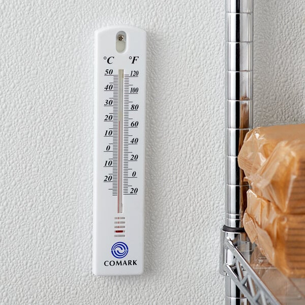 A Comark indoor/outdoor wall thermometer on a wall.